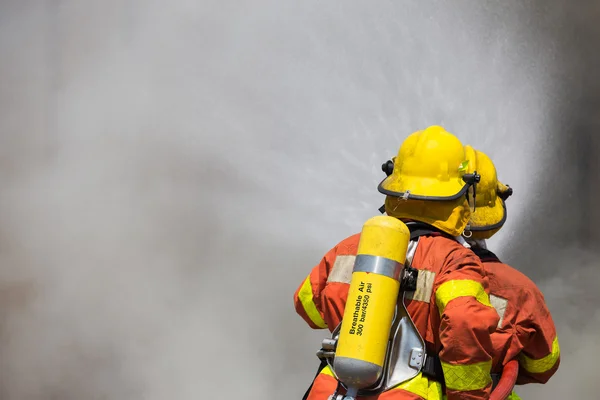 Dos bomberos en traje de extinción de incendios rociando agua al fuego y — Foto de Stock