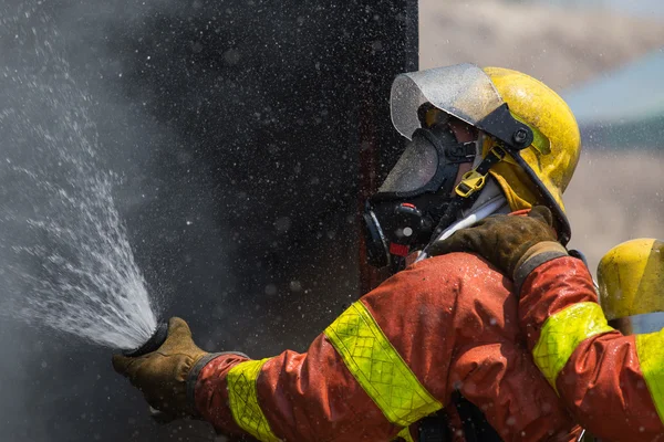 Pompiere in tuta antincendio spruzzare acqua al fuoco circondano wi — Foto Stock