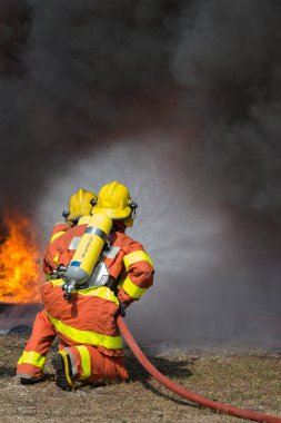 2 firemen spraying water in fire fighting with fire and dark smo clipart