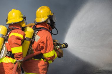 2 firefighters spraying water in fire fighting with dark smoke b clipart