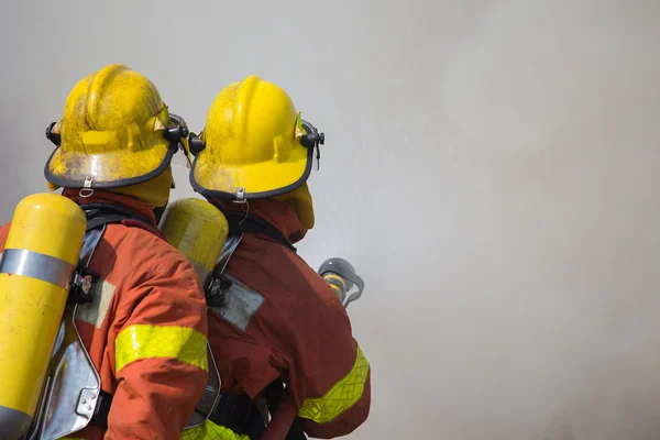 2 firemen spraying water in fire and smoke — Stock Photo, Image