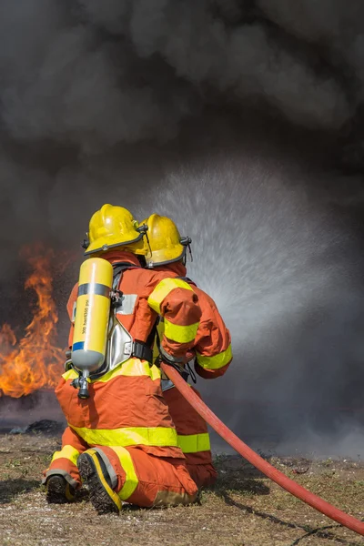 2 pompieri che spruzzano acqua nel fuoco combattendo con fuoco e buio smo — Foto Stock