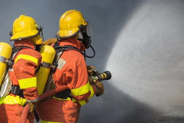 2 bomberos rociando agua en la lucha contra el fuego con humo oscuro b —  Fotos de Stock