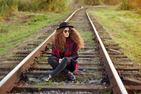 Una chica se sienta sobre rieles en el soleado clima otoñal — Foto de Stock