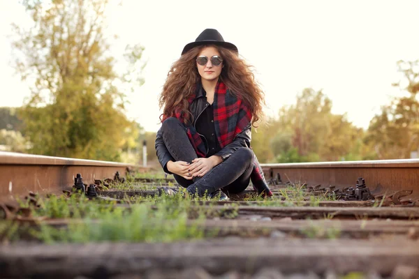 Chica en un sombrero sentado en las pistas en un clima soleado de otoño — Foto de Stock