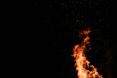 Yerde yakacak odunları olan ateş. Kırmızı alevler. Güzel kıvılcımlar saçan siyah arka plan..