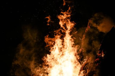 Yerde yakacak odunları olan ateş. Kırmızı alevler. Güzel kıvılcımlar saçan siyah arka plan..