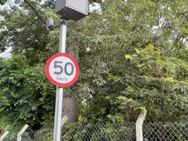 Sarı oklu trafik levhası ve vahşi doğanın bulanık arka planına sahip bir direkte sabit hız kameraları..