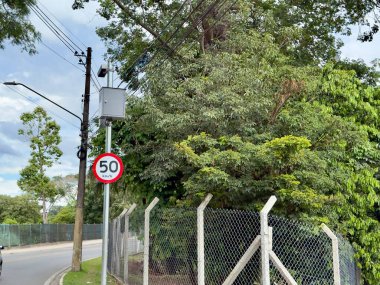 Sarı oklu trafik levhası ve vahşi doğanın bulanık arka planına sahip bir direkte sabit hız kameraları..