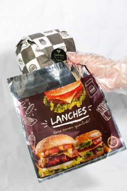 Hamburger teslimatı için termal paket tek kullanımlık eldivenle tutuluyor. Paket yemek, fast food, hijyen, gıda güvenliği ve modern dağıtım hizmeti kavramı.