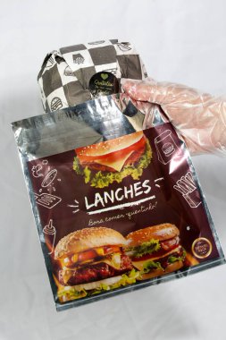 Hamburger teslimatı için termal paket tek kullanımlık eldivenle tutuluyor. Paket yemek, fast food, hijyen, gıda güvenliği ve modern dağıtım hizmeti kavramı.