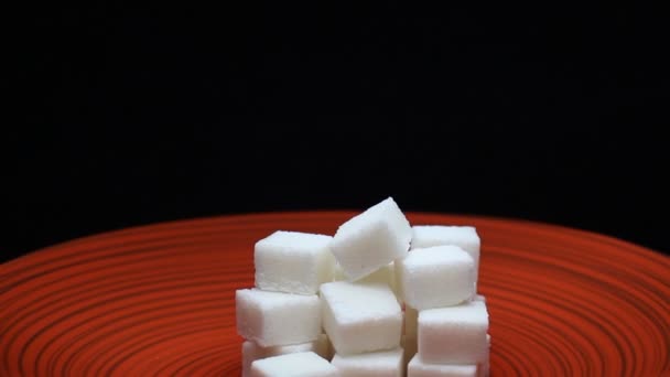 Cubos de azúcar en una placa roja Fondo negro giratorio — Vídeo de stock
