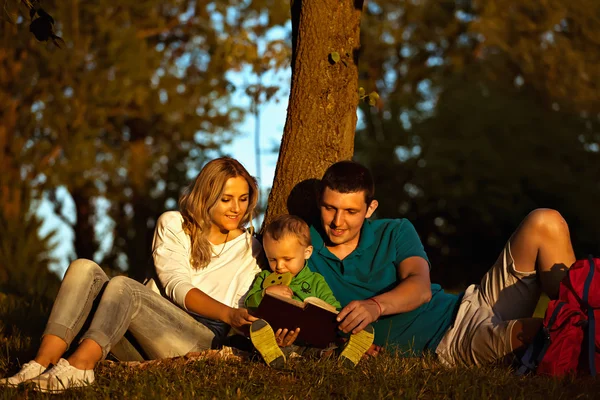 Familia joven feliz en el picnic en el parque leyendo el libro . —  Fotos de Stock