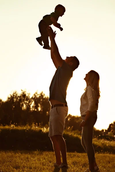 Silueta de familia feliz al atardecer en el parque o jardín . —  Fotos de Stock