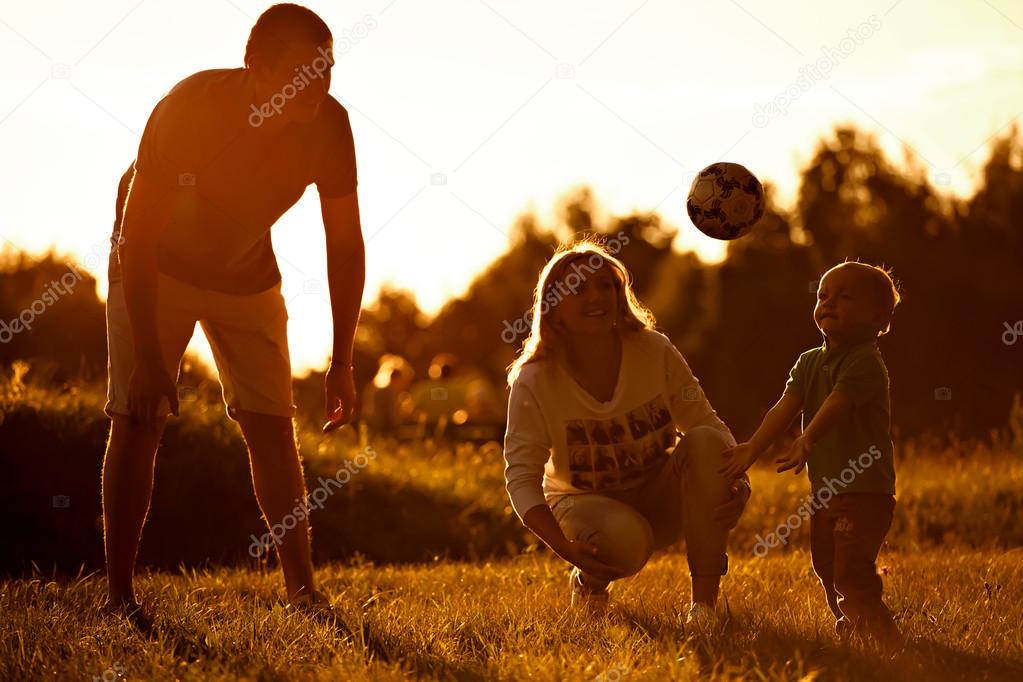Happy mother and father play with their little son in football.
