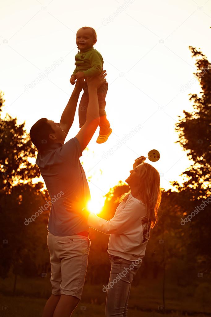 Happy young parents with little son smilling, having fun and relaxing together in park.