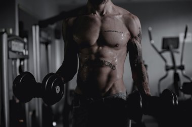 Islak seksi kaslı adam dumbbells tutan spor salonunda.