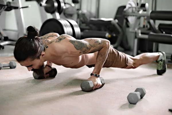 Jeune athlète musclé faisant des pompes dans la salle de gym . — Photo