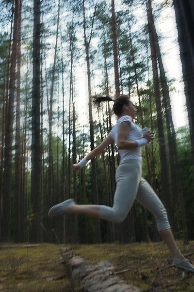 Junge Fitness-Frau läuft und springt beim extremen Outdoor-Fitnesstraining im Wald über Baumstämme. Stockbild