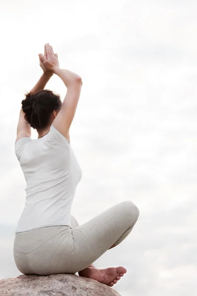 Yoga genç kadının lotus poz taş üzerinde oturan kolay egzersizler yapması.