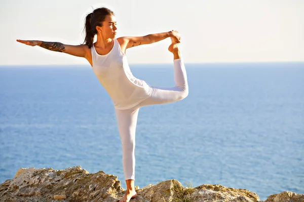 Slim atletische jonge meisje doet yoga op de rotswand op de achtergrond van blauwe zee. — Stockfoto