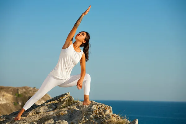 Female yoga model working out training on the top of mountain on background of sea. Royalty Free Stock Images