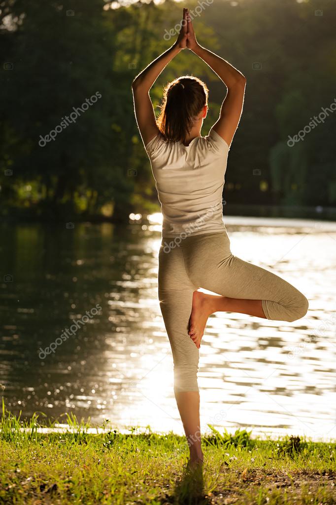 Young woman practicing tree yoga pose near the river during sunset or sunrise.