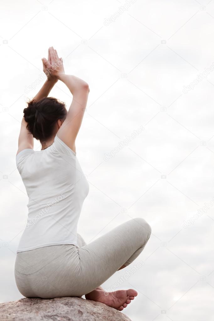 Yoga young woman doing easy exercises sitting in lotus pose on stone.