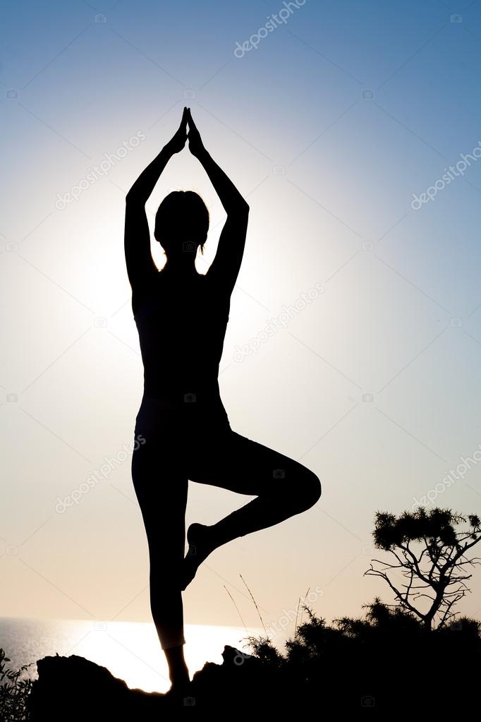 Silhouette of a slender fitness yoga girl in the sun at sunset or sunrise in tree pose.