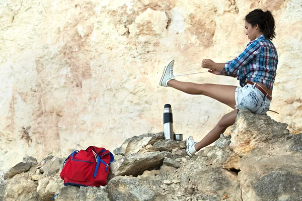 Hiker with backpack sitting on top of the mountain and tying shoelaces. Stock Picture