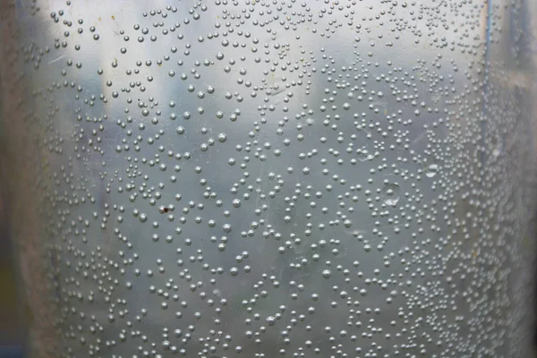 Small, round, spherical bubbles covered the surface of a plastic container of water. Mysterious and unusual light background.