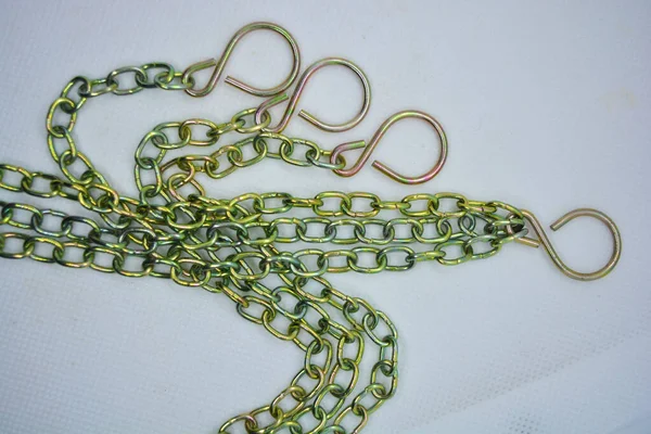 Metal chains, overflow chains and large hooks are arranged randomly on a white fabric background.