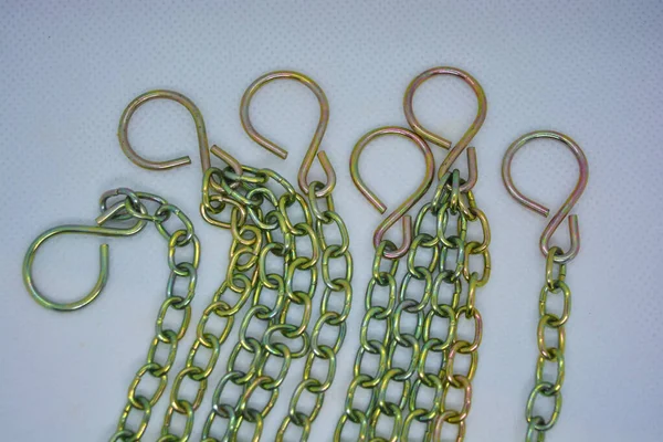 Metal chains, overflow chains and large hooks are arranged randomly on a white fabric background.