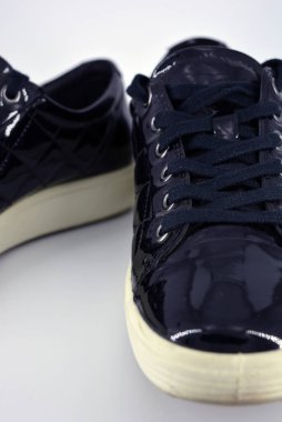 Stylish bright black lacquer shoes located on a white background. Moccasins made of genuine leather with bullshit and black wide laces. Women's sneakers on a white tast sole. 