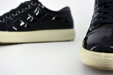 Stylish bright black lacquer shoes located on a white background. Moccasins made of genuine leather with bullshit and black wide laces. Women's sneakers on a white tast sole. 