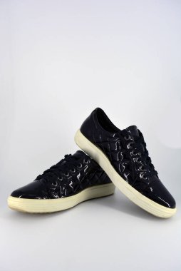 Stylish bright black lacquer shoes located on a white background. Moccasins made of genuine leather with bullshit and black wide laces. Women's sneakers on a white tast sole. 