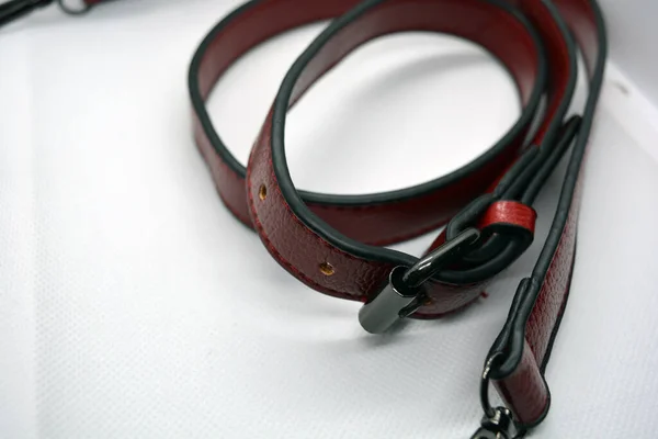 Red leather belt with metal buckle. Leather accessory ribbon chaotically scattered on a white background. Beautiful skin with shimmering and fringes.