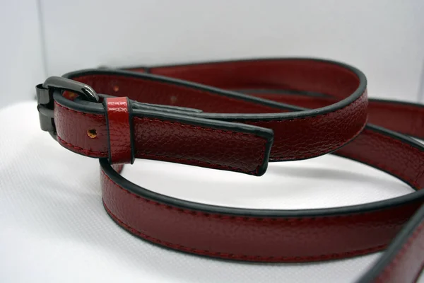 Red leather belt with metal buckle. Leather accessory ribbon chaotically scattered on a white background. Beautiful skin with shimmering and fringes.