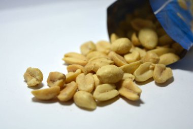 Lezzetli kavrulmuş kabuklu fıstık, beyaz bir tabağa tuz serpiştirilmiş, dağınık ve mavi politen ambalajdan dökülmüş..