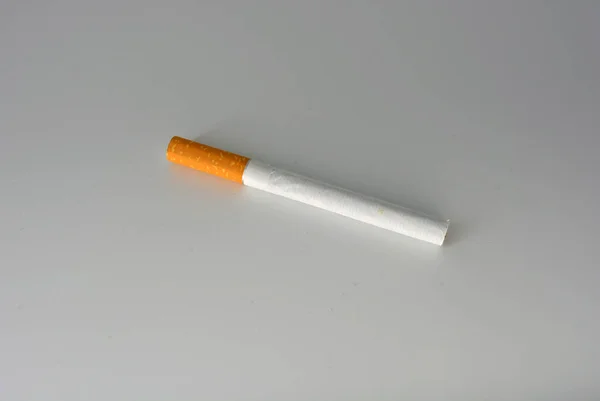 One white cigarette with brown filter located on a white background. Smoking is blicking bad on health. Cigarettes worsen the work of the brain nerves.