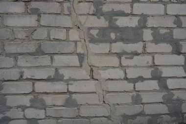 Construction renovation work, old wall with problems, flaws. Many large cracks in white brick wall, problem areas filled with cement that had fallen off. Poor, substandard construction work.