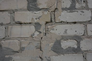 Construction renovation work, old wall with problems, flaws. Many large cracks in white brick wall, problem areas filled with cement that had fallen off. Poor, substandard construction work.
