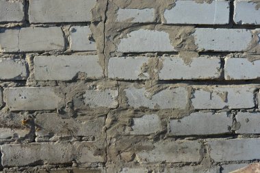 Construction and renovation work, a wall with imperfections and unevenness, the first masonry. A wall of white brick, gray cement, illuminated by the rays of the sun.