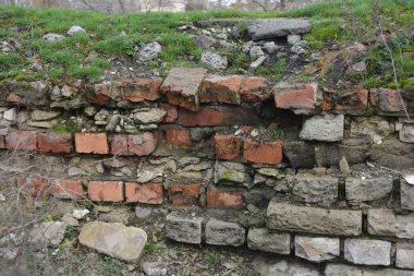 Açık gri bir duvar, eski bir bina, yeşil yosun ve nemli bir çit. Açık gri, kırmızı tuğlalar, güzel, şık tuğlalar..