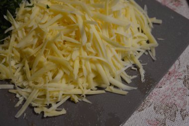 Yemek, bakkaliye, yemek. İki büyük parça doğranmış yeşil maydanoz ve beyaz, şeritler halinde kesilmiş sarı Gouda peyniri gri bir plastik kesme tahtasına yerleştirilmiştir..