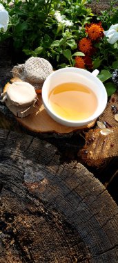 Bir jüt kumaş, ıhlamur çiçekleri, iki kavanoz bal ve ıhlamur çiçekli bir fincan çay.