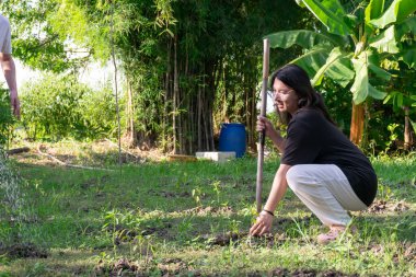 İki Taylandlı LGBTQ arkadaşı yeşil arka bahçede bahçıvanlık yapıyor. Biri toprağı gevşetmek için çömeliyor ve gülümsüyor. Bu sırada sıcak akşam güneşi altında başka bir sulama bitkisi de huzurlu, basit bir hayatı simgeliyor.