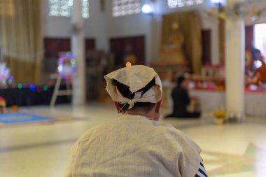 Suphanburi, Tayland - 7 Kasım 2025: Basit giysili bir insan Budist cenazesinde oturur. Keşişler, Tayland Song Barajı ve Lao geleneklerini harmanlayan bir törenle ilahiler söylüyor..