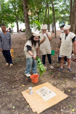 Suphanburi, Tayland - 7 Kasım 2025: Basit kenevir yas giysileri içindeki aile üyeleri ağaçlık bir bölgede sakin bir saygı ile Budist Tayland Black Thai kemik toplama ayini düzenledi.