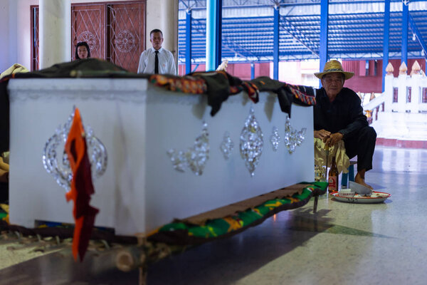 Suphanburi, Thailand - November 7, 2025 : A traditional Thai Song Dam funeral ritual, with mourners in simple white clothes, offering prayers during the final rites, guided by the elder near coffin.